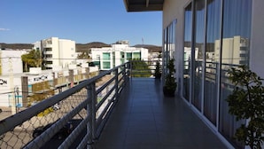 Uma varanda com cerca de arame, plantas em vasos e vista para edifícios ao fundo.