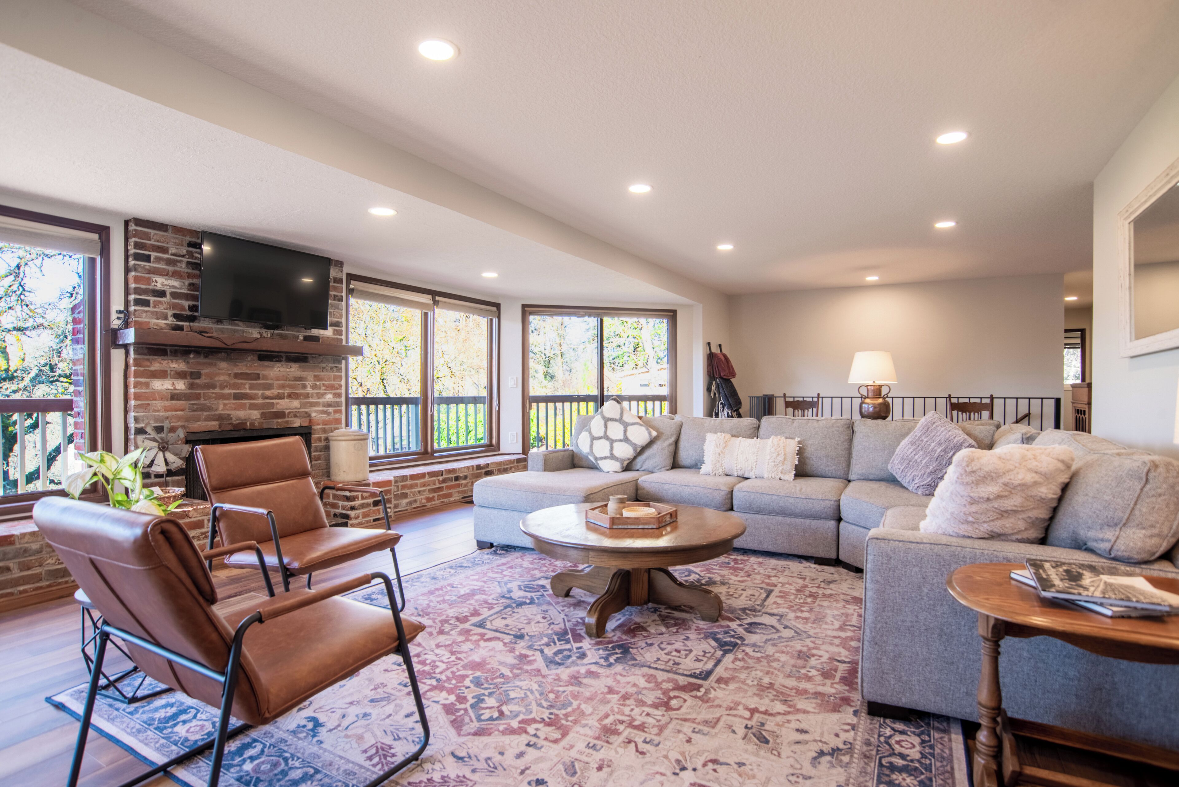A spacious living room with a brick fireplace, a large grey sofa, a leather chair, and a round coffee table.