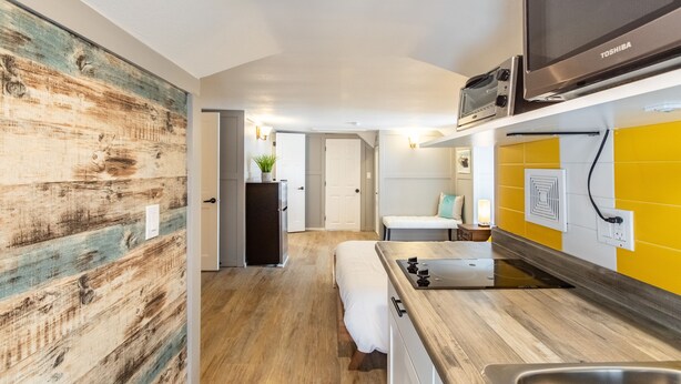 A compact kitchen with a microwave, stove, and sink. A small refrigerator and a bench are also visible. - 8037-Walk to Mayo- Loft apt in the middle of Mayo campus (Rochester)
