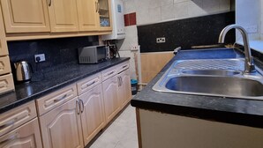 A kitchen with wooden cabinets, a black countertop, a stainless steel sink, and a microwave. - 3 Bedroom House in Central Rochdale cul-de-sac Free Parking & Fast Wi-Fi (Rochdale)