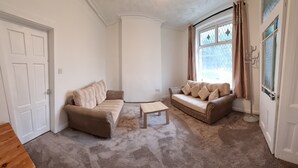 A living room with two beige sofas, a wooden coffee table, and a carpeted floor. - 3 Bedroom House in Central Rochdale cul-de-sac Free Parking & Fast Wi-Fi (Rochdale)