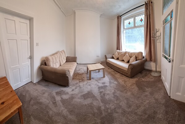A living room with two beige sofas, a wooden coffee table, and a carpeted floor.