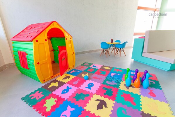 A play area with a colorful playhouse, a foam mat with animal shapes, and a table with chairs.