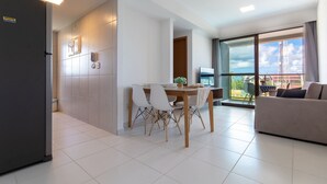 A modern kitchen with a refrigerator, a dining area with a table and chairs, and a balcony with a view. - Mana Beach Muro Alto C301 - Carpediem (Ipojuca)