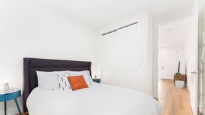 Ein Schlafzimmer mit einem großen Bett, einem Nachttisch, einer Kommode und einer Tür zu einem anderen Raum.