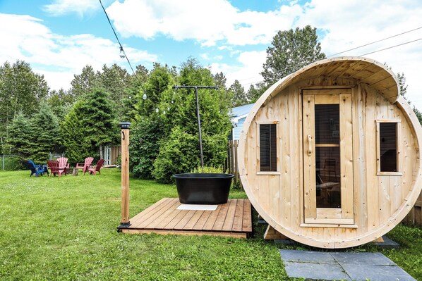 A wooden cabin with a large circular door, a hot tub, and outdoor seating.