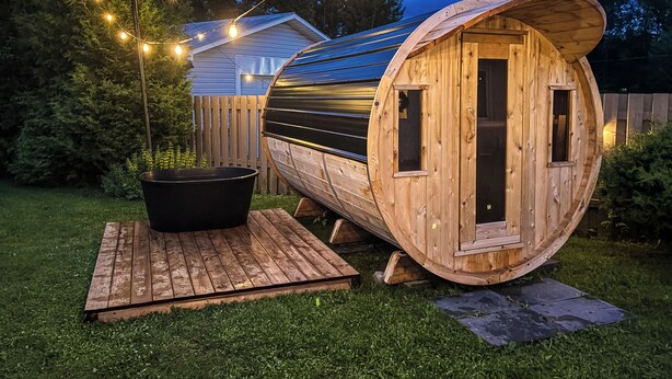 Een houten cilindervormige constructie met een deur, een tuinhuisje en een hottub in een achtertuin.