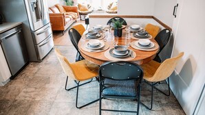Een eethoek met een ronde tafel gedekt voor zes personen, omringd door zes stoelen, in een moderne keuken met een koelkast en kastjes.