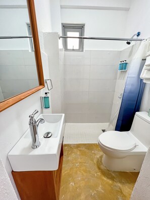 Een badkamer met een wit wastafel, toilet, douche en een klein raam.