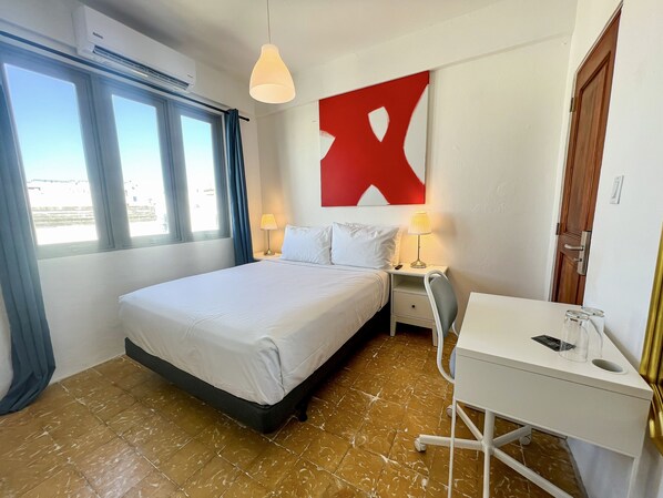 A hotel room with a bed, bedside tables, a desk, and a large window. - Bahia Urbana Hotel (San Juan)