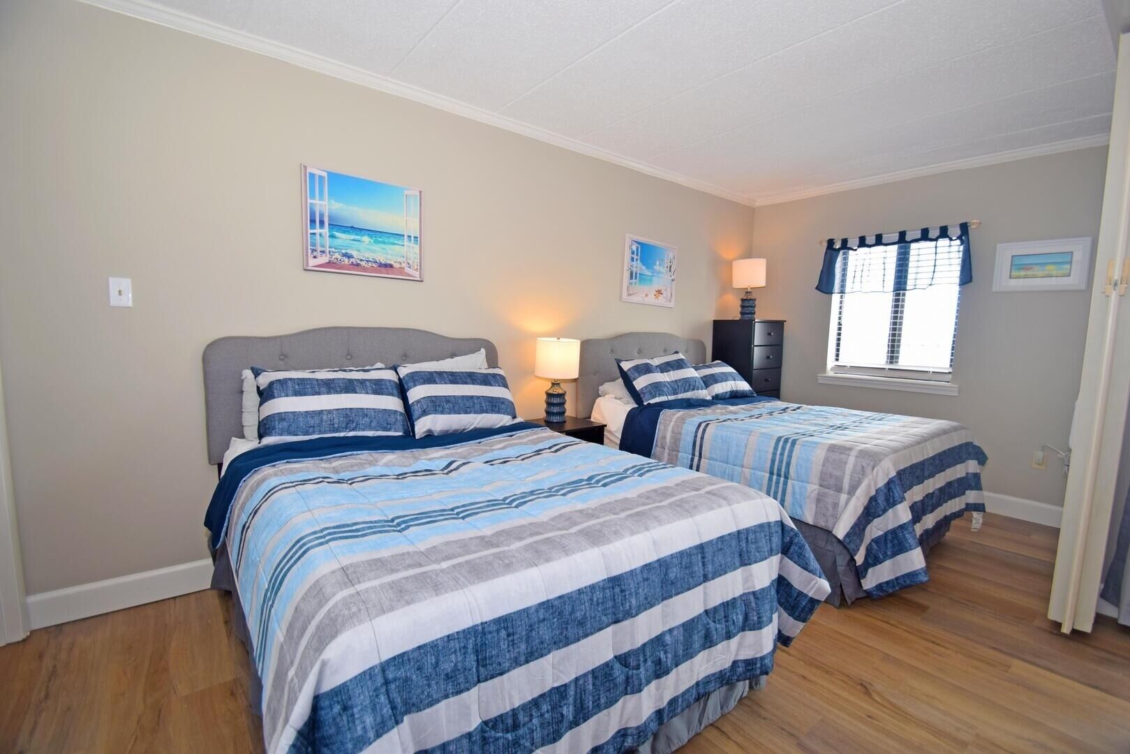 Een slaapkamer met twee bedden, elk voorzien van gestreept beddengoed, een nachtkastje met een lamp en een raam met gordijnen.