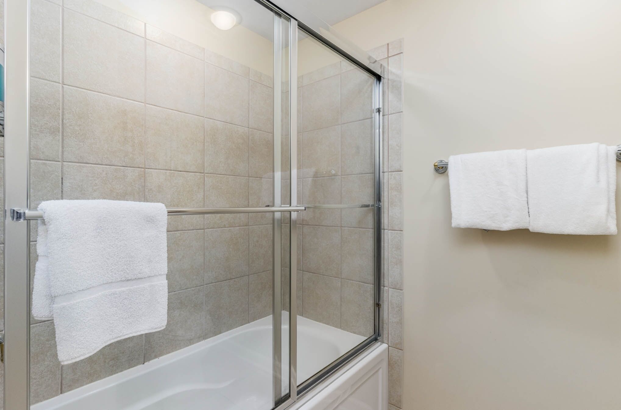 A shower area with a glass door, a white bathtub, and a towel rack with two white towels.