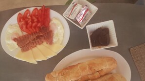 En tallerken med æg, bacon, ost og tomater, samt et baguettebrød på et bord.
