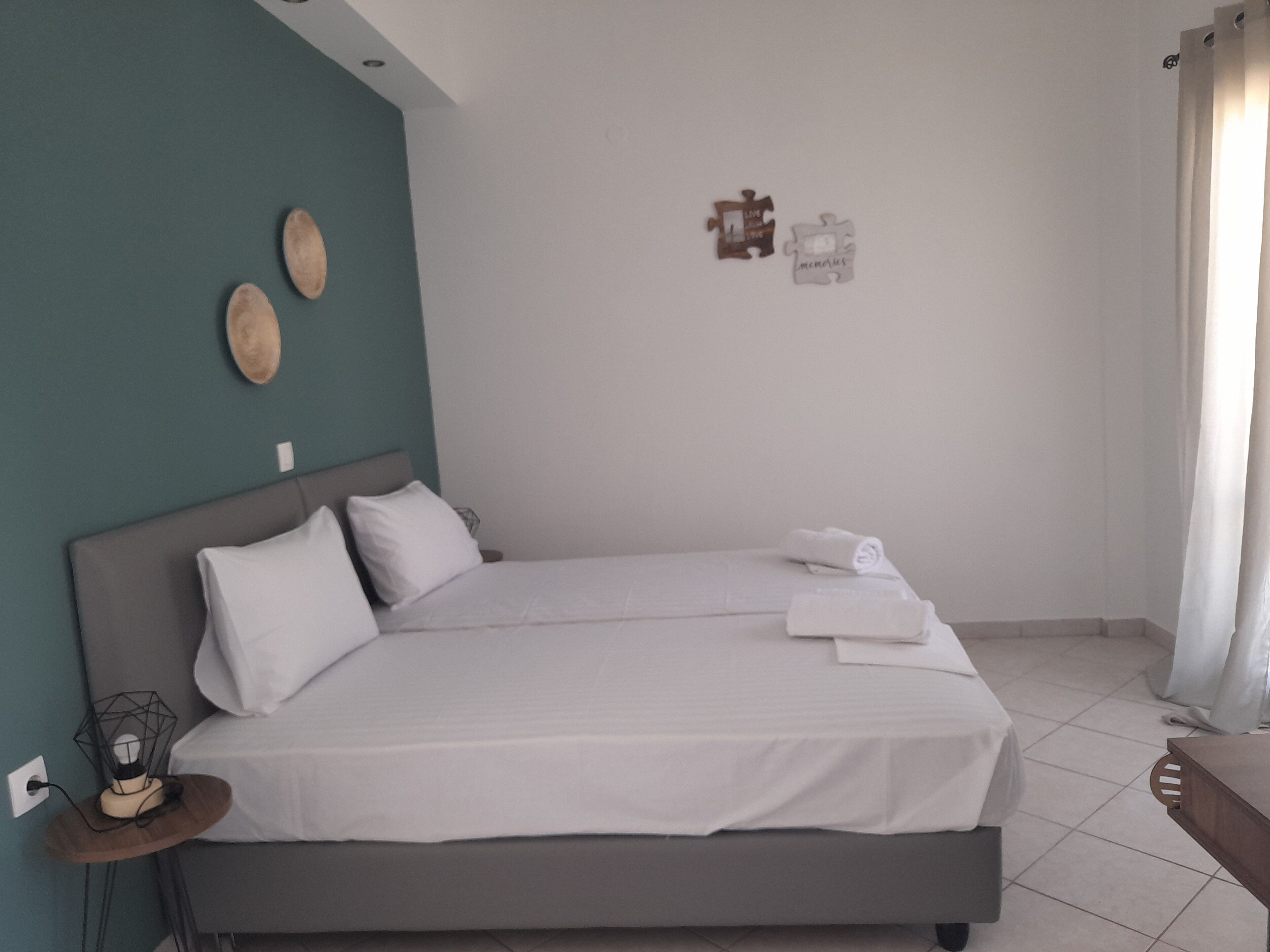 A bedroom with a bed, pillows, a bedside table with a lamp, and a wall with two decorative items.