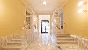 Un escalier en marbre, avec des rampes blanches, mène à une porte située au fond.
