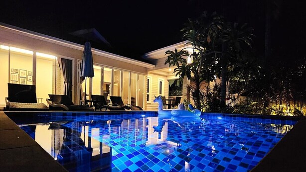 Vue nocturne d’une piscine aux carreaux bleus, entourée d’un patio bien éclairé, agrémenté de chaises longues et de parasols.