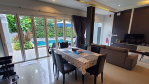 Un salon moderne comprenant un coin repas, un canapé, un téléviseur et une vue sur une piscine, visible à travers de grandes portes coulissantes.