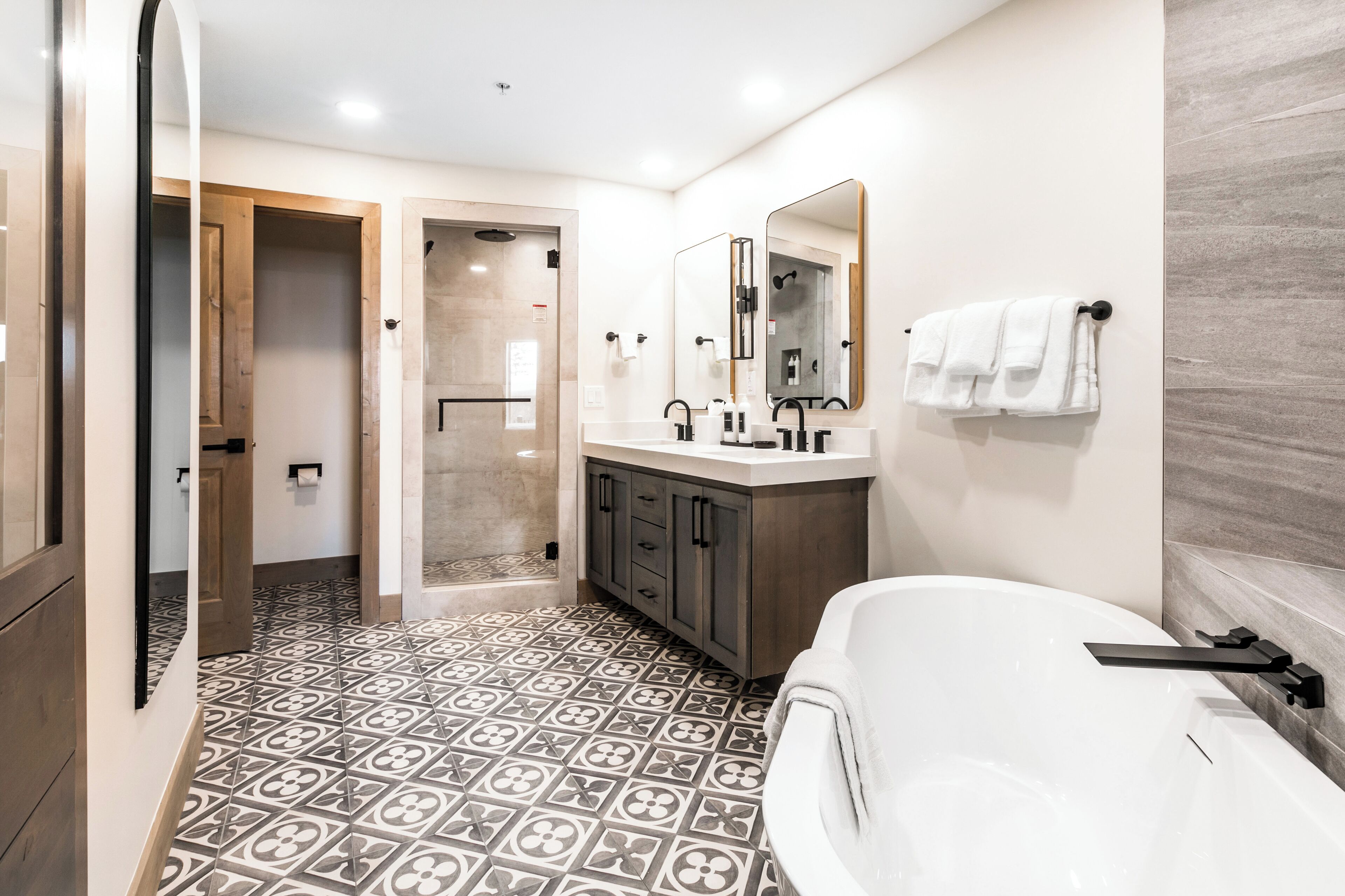 A modern bathroom with a freestanding bathtub, a double vanity with a mirror, and patterned floor tiles.