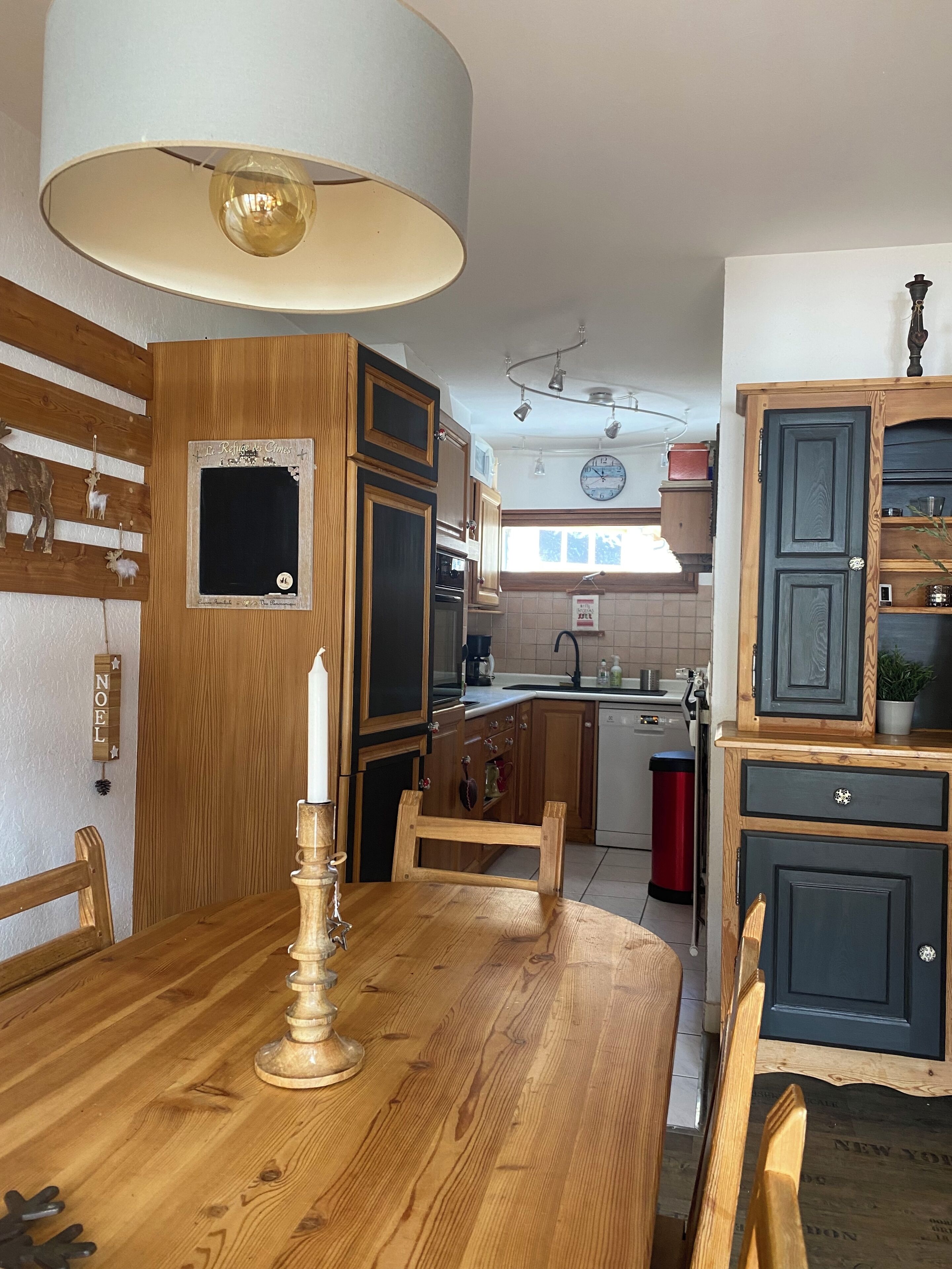 Une cuisine avec des meubles en bois, une table à manger éclairée par une bougie et une horloge au mur.