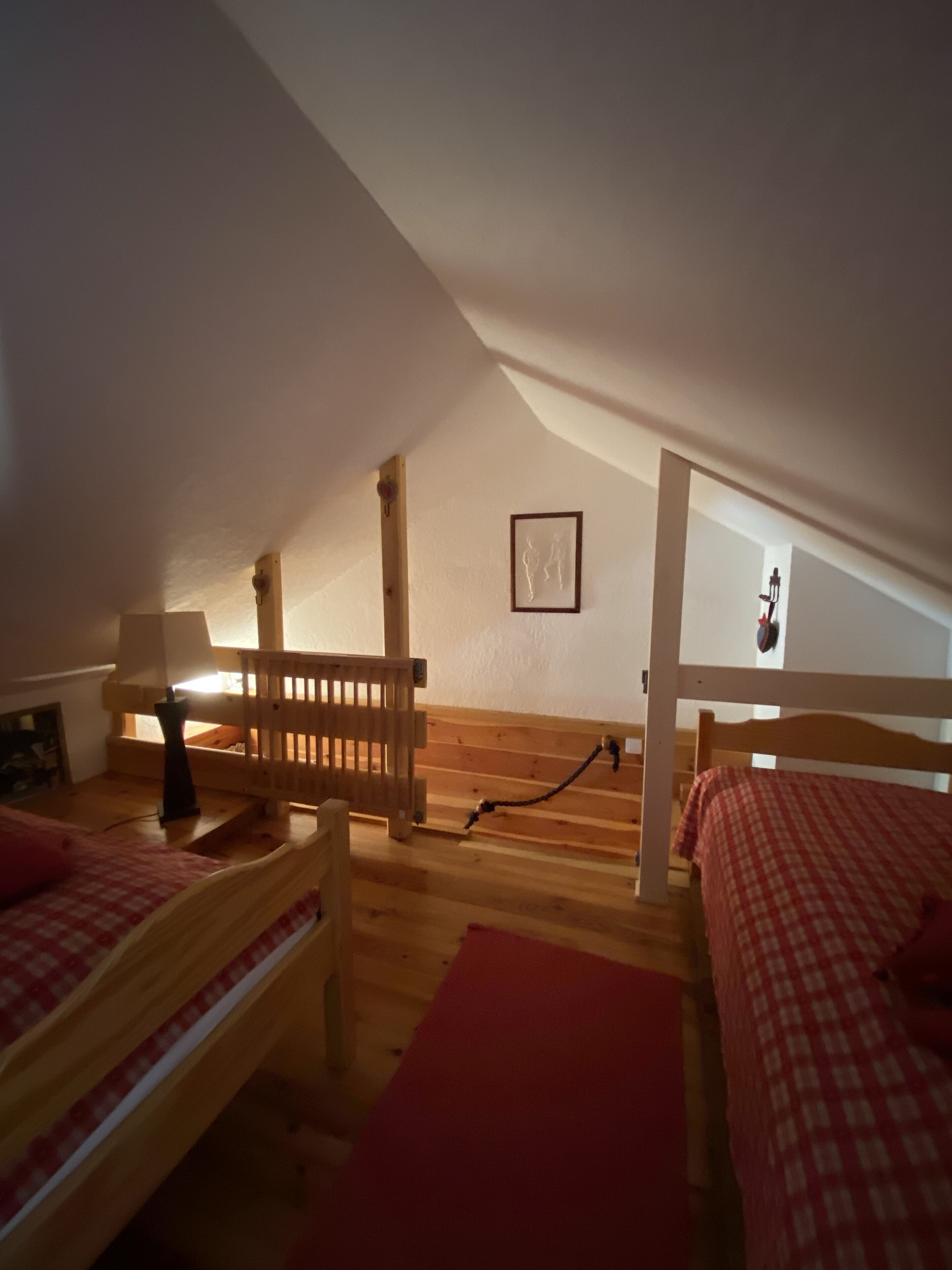 Ein gemütliches Schlafzimmer unter dem Dach mit Holzbettställen, einem kleinen Tisch und einem gerahmten Bild an der Wand.