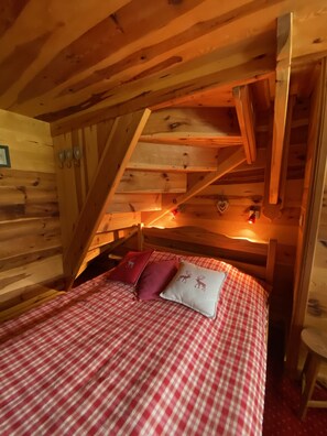 Une chambre dans une cabane en bois, avec une couverture à carreaux, un escalier en bois et un mur en bois.