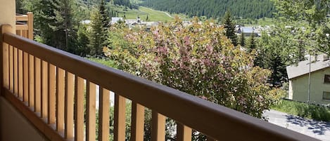A balcony with a wooden railing overlooking a mountainous landscape with a valley and a small village.