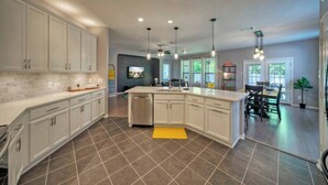 A modern kitchen with white cabinets, a central island, and a dining area with a table and chairs. - 🔆 Sunny Delight of Pville 🔆 (Pflugerville)