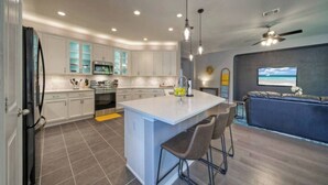 A modern kitchen with white cabinets, a central island with bar stools, and a dining area with a sofa and a ceiling fan. - 🔆 Sunny Delight of Pville 🔆 (Pflugerville)