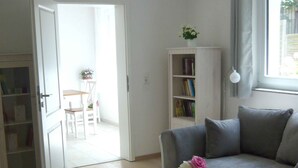 A living room with a sofa, a wooden coffee table with a book and flowers, a bookshelf, and a door leading to another room. - 3-room vacation apartment in the Allgäu with garden and wood-burning stove (Leutkirch im Allgäu)