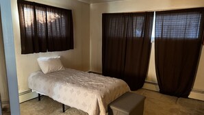 A bedroom with a bed, a bench, and two sets of curtains.