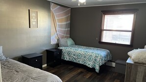 A bedroom with two beds, a ceiling fan, a window with blinds, and a motivational quote on the wall.