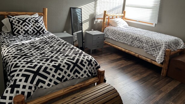 A bedroom with two wooden beds, a bedside table, a mirror, and a window with blinds.