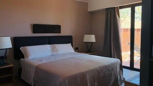 Una camera d'albergo con un letto grande, un comodino con una lampada, una finestra con tende e vista sull'esterno.