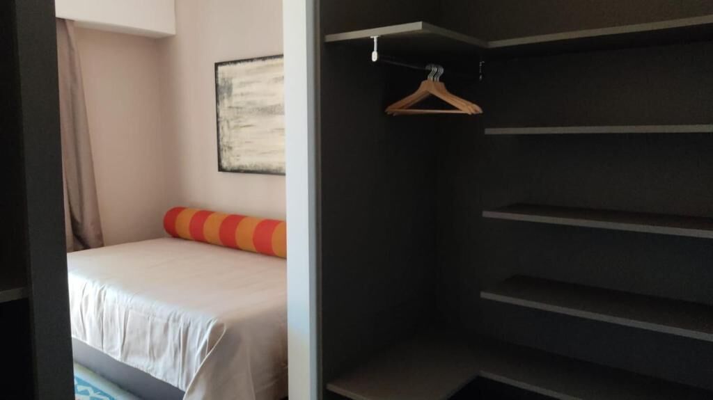 A hotel room with a bed, a hanging coat rack, and a framed picture on the wall.