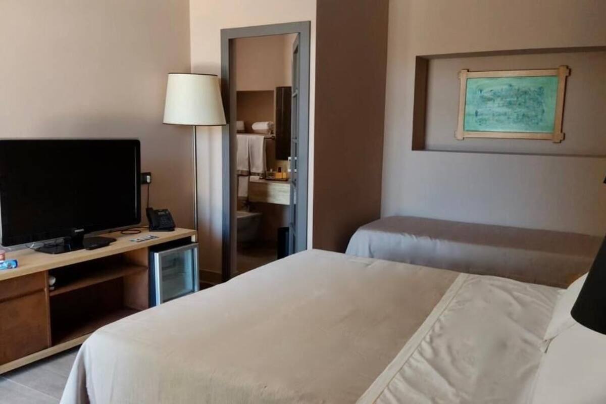 Een hotelkamer met een bed, een bureau met een televisie, een lamp en een lijst met een afbeelding aan de muur.