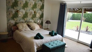 A bedroom with a large bed, a bench, a lamp, and a view of a garden through a sliding door.
