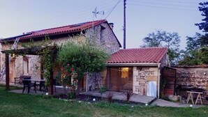 A rustic stone house with a red-tiled roof, a small garden, and outdoor furniture.
