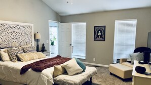 A bedroom with a bed, a desk, a chair, a ceiling fan, and a door leading to another room. - The Nash Spot (Nashville)