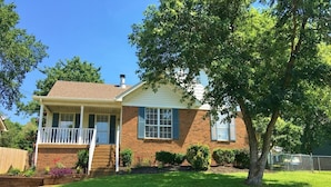 A single-story house with a front porch, brick exterior, and a well-maintained lawn. - The Nash Spot (Nashville)
