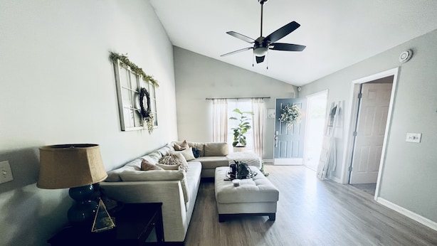 A spacious living room with a sofa, ottoman, and a ceiling fan. - The Nash Spot (Nashville)