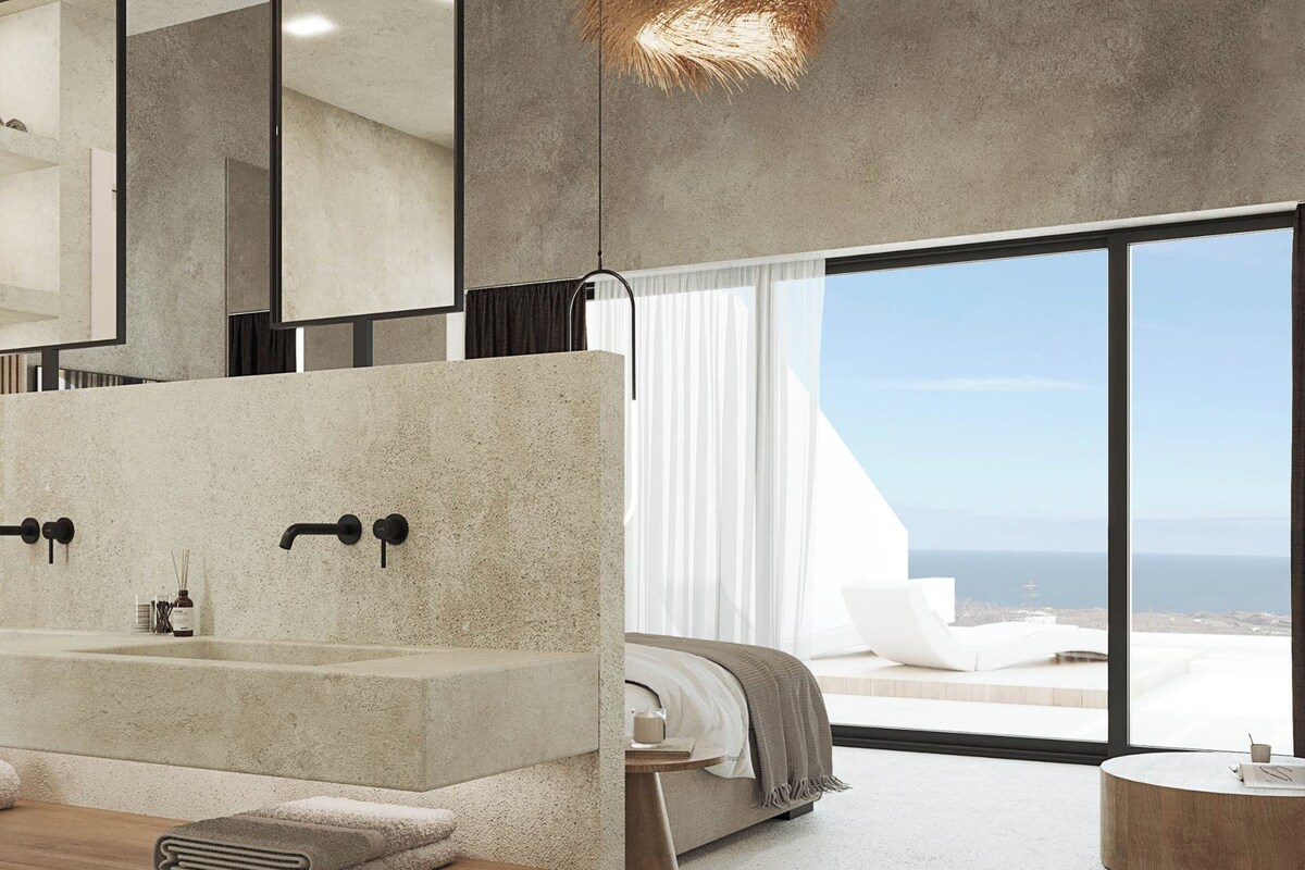 A modern bathroom with a large sink, mirror, and a view of the sea.