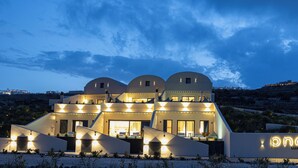A modern building with multiple domed structures, a sign reading "pné Luxury Suites," and a landscaped area in front. - Pnoé Luxury Suites (Santorini)