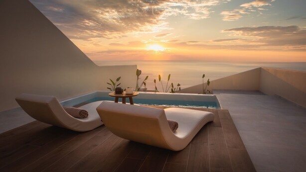 A modern rooftop terrace with two lounge chairs, a small table, and a pool, overlooking a sunset over the sea. - Pnoé Luxury Suites (Santorini)