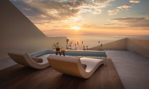 Een modern terras op het dak met twee loungestoelen, een kleine tafel en een zwembad, met uitzicht op een zonsondergang boven de zee.