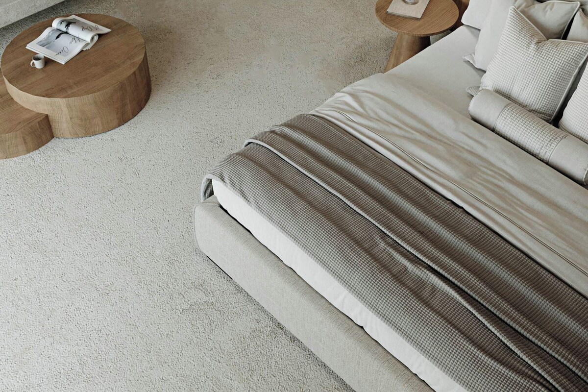 A bedroom with a large bed, two round wooden side tables, a magazine, and a cup on one table.