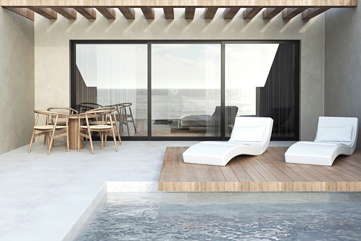 A modern outdoor seating area with a wooden table and chairs, two white lounge chairs, and a large sliding glass door leading to an interior space.