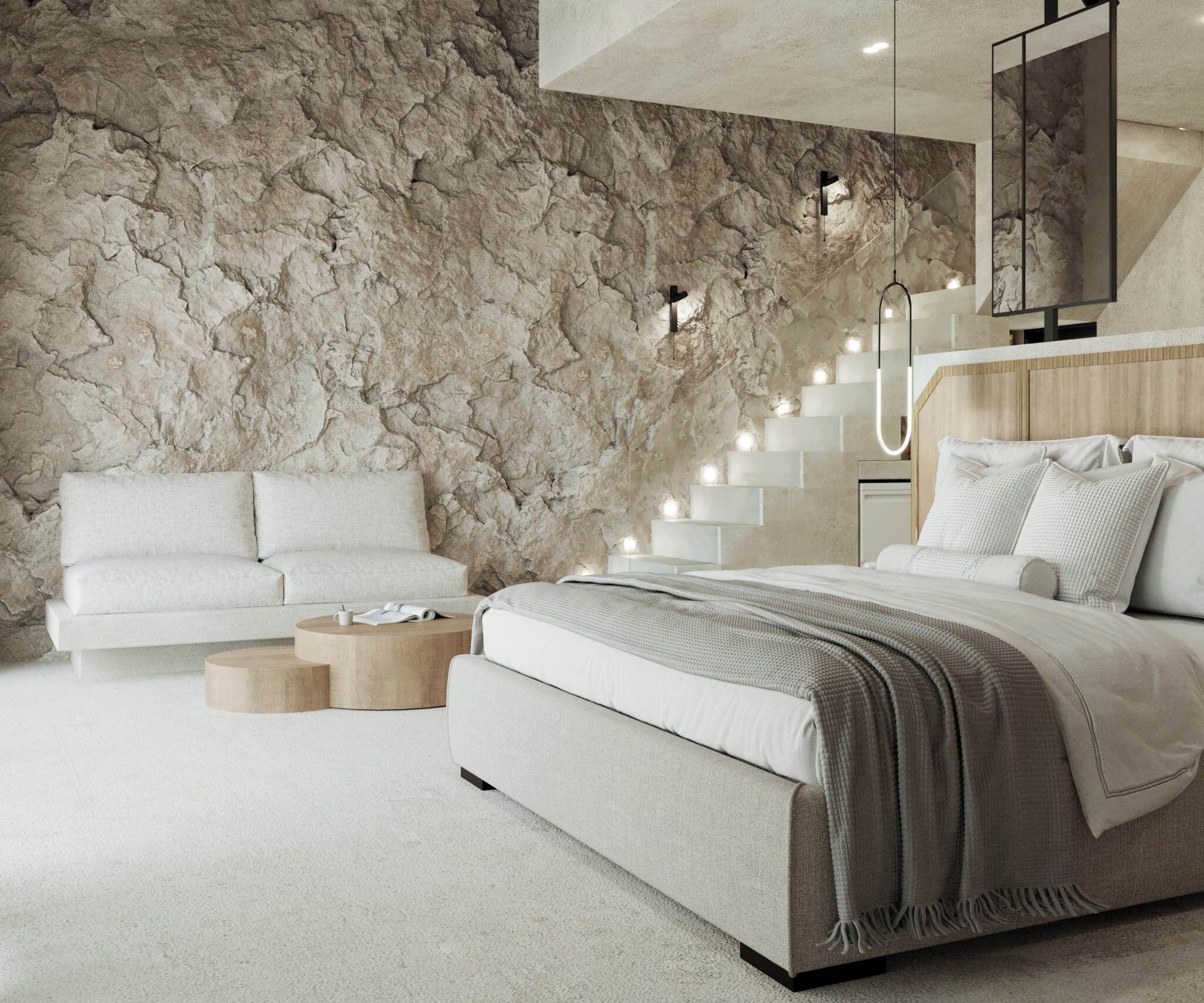 A bedroom with a large bed, a white sofa, a wooden coffee table, and a stone wall.