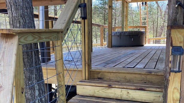 A wooden deck with a metal railing, a staircase, and a covered area with a bench.