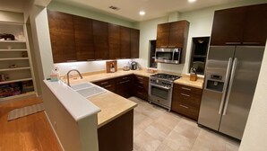 Une cuisine moderne avec des meubles en bois foncé, des appareils électroménagers en acier inoxydable et un plan de travail de couleur beige.