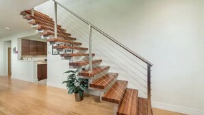 Un escalier moderne avec des marches en bois et une rampe en métal, menant à un espace cuisine équipé de placards et d’un plan de travail.